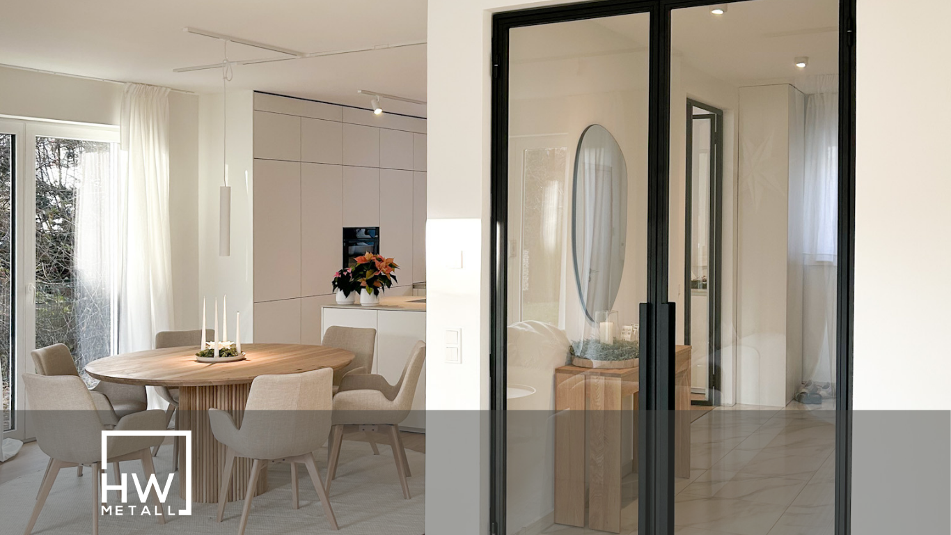Moderner Wohnraum mit industriellem Flair, durch eine schwarze Loft-Schiebetür mit Glaseinsätzen vom angrenzenden Zimmer getrennt. Helle Wände, Holzfußboden und minimalistisches Interieur betonen den offenen, urbanen Stil.